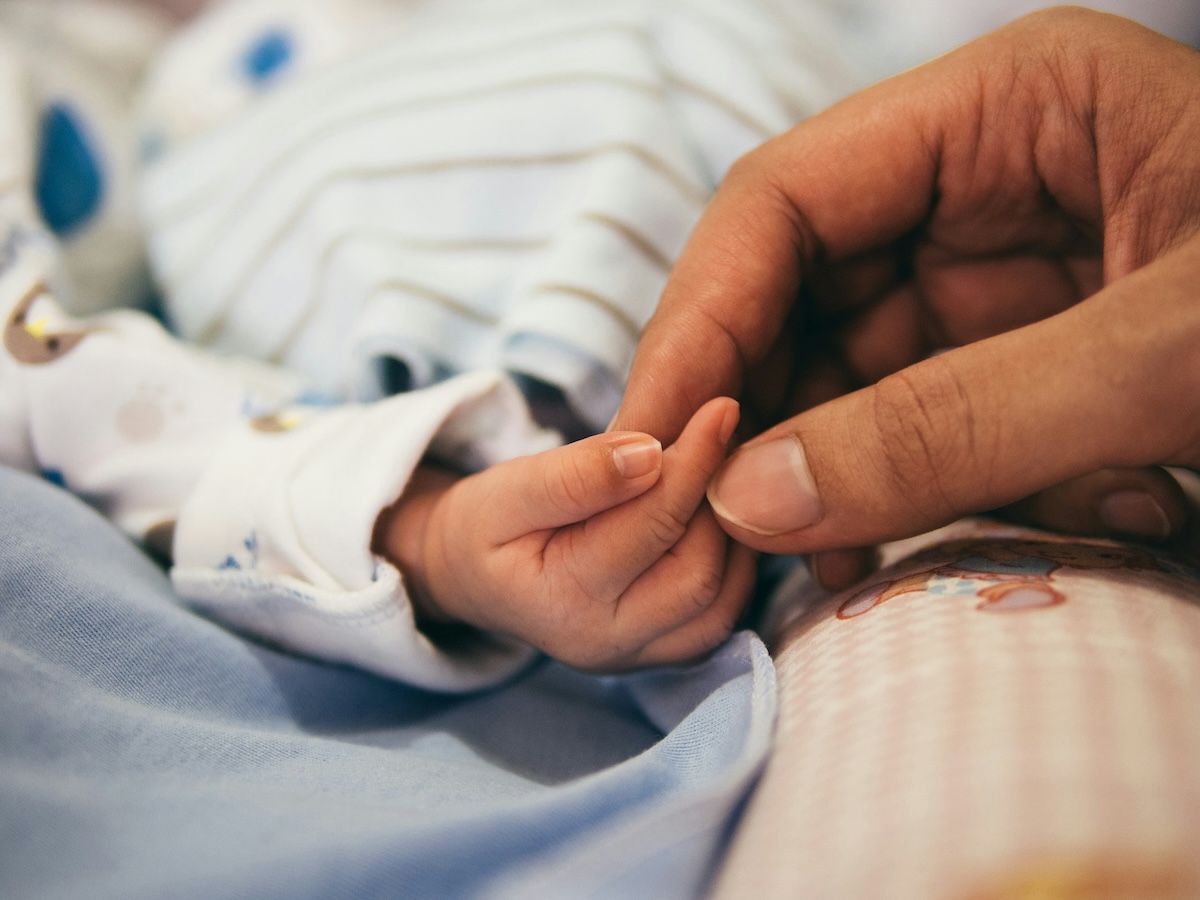 Photo of a small newborn baby&rsquo;s hand wrapped around an adult&rsquo;s finger